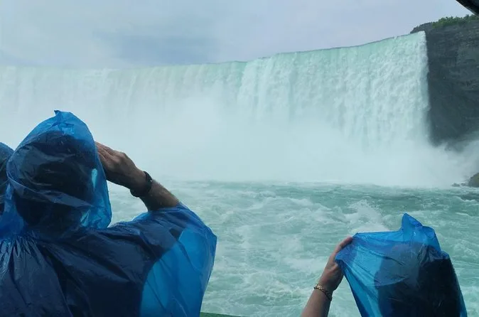 Besucher in blauen Ponchos fotografieren vom Boot aus einen Vorhang aus herabstürzendem Wasser