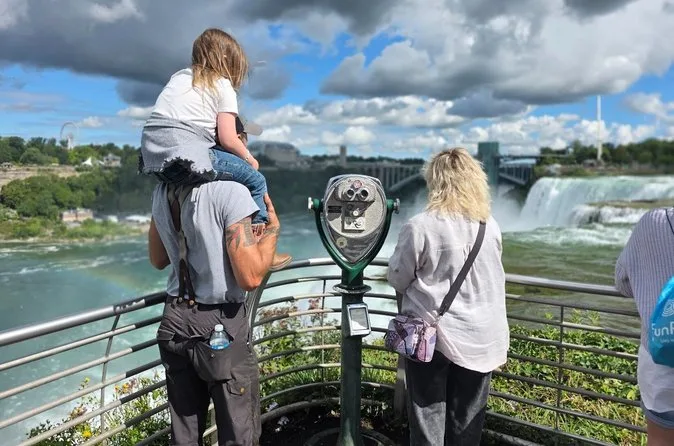 Ein Kind auf den Schultern eines Elternteils an einem Aussichtsgeländer über dem Fluss
